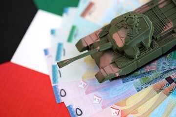 Kuwaiti dinar currency money bills and toy tank on flag. The concept of army funds and weapons sales