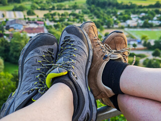 Two people are sitting on a fence, one wearing a gray and yellow shoe