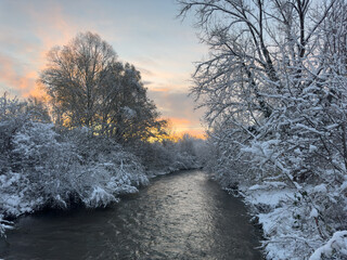 Winter river flowing through snowy forest at dusk