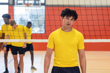Diverse male volleyball partners in yellow shirts practicing strategy behind net on polished court