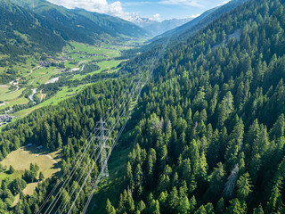 Aerial view of power line pylon in mountaineous area in Switzerland through valley in Canton of Valais.