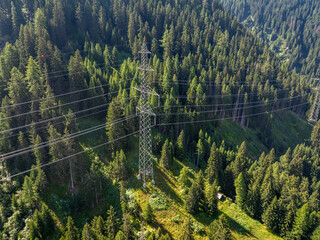 Aerial view of power line pylon in alpine forest in Switzerland. Electric current distribution with power grid.