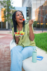 Happy black woman eating fresh salad outdoors in a modern city