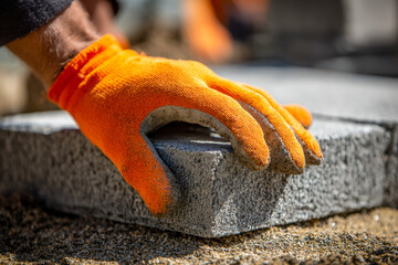 Worker placing a concrete block with protective orange gloves on a construction site