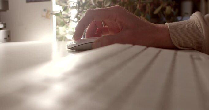 A hand skillfully maneuvers a sleek computer mouse on a polished wooden desk, softly illuminated, with vibrant green plants in the background creating a calming atmosphere for productivity