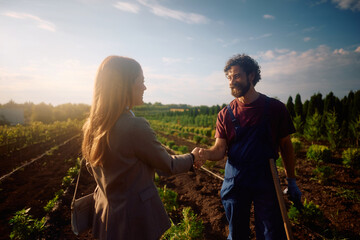 Happy plant nursery worker shaking hands with a businesswoman in the field.