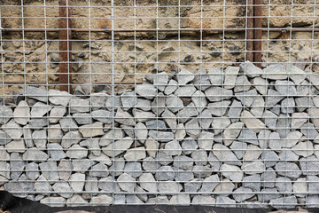 Stone fence in steel mesh and green lawn. Close up of gabion with tightly packed stones of varying...