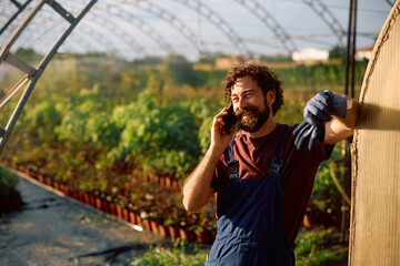 Happy farm owner making a phone call while working in a greenhouse.