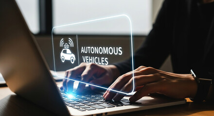 Person typing on laptop with autonomous vehicles graphic overlay showing on the screen display