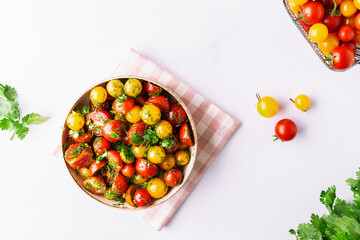 Bright juicy salad with colorful cherry tomatoes and aromatic herbs on white marble table top view. Healthy vegan food concept. 