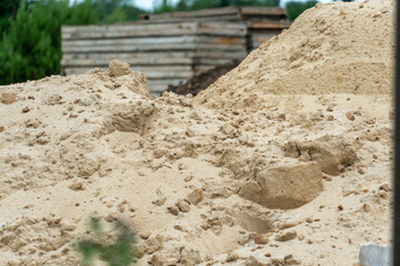 Construction site features large piles of sand and gravel beside wooden materials on a cloudy day