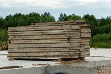 Stacked wooden planks resting on a construction site near a forest under cloudy skies