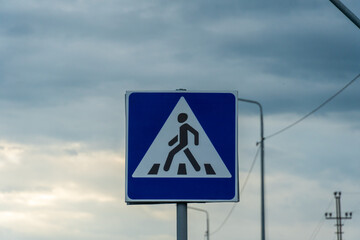 Pedestrian crossing sign under a cloudy sky signals caution for travelers in an urban area