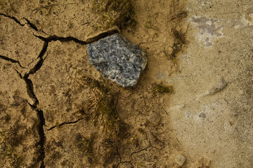 Abstract background of cracked dry earth and a grey stone. Top-down view showcasing natural...