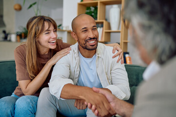 Happy couple shaking hands with financial advisor during a meeting at home, smiling and making a...