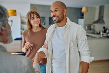 Fototapeta premium Happy couple shaking hands with a real estate agent inside their new home, joyfully celebrating the moment of receiving keys