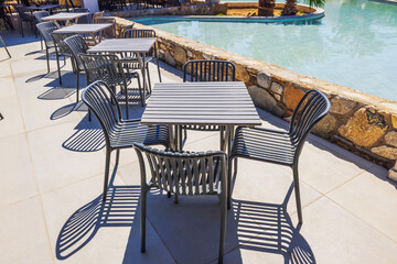 Close up view of outdoor restaurant terrace with black chairs and tables beside pool in sunny...