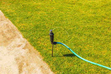 Close up view of garden sprinkler watering green lawn with hose connection in sunny outdoor...