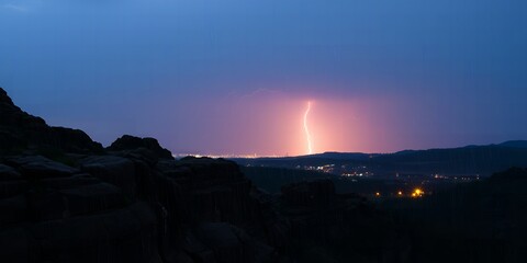 Dramatic lightning illuminates a distant cityscape during a nighttime thunderstorm over hilly terrain