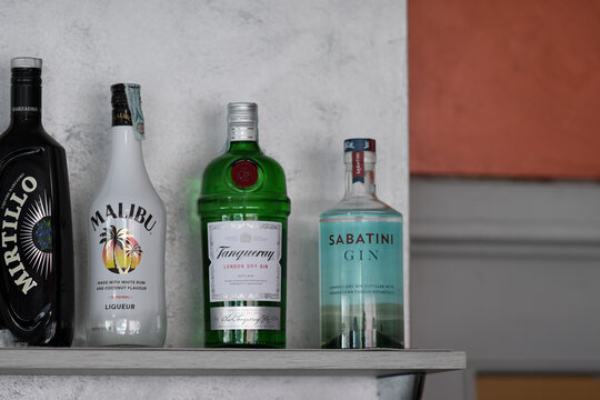 Mirtillo, Malibu, Tanqueray, and Sabatini gin bottles lined up on wooden bar shelf, waiting for mixology magic at nighttime
