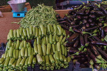 Fresh green zucchini and purple eggplants arranged at vibrant farmers market stall with traditional...