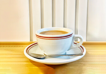 Hot milk tea or karak chai with spoon served in white cup isolated on wooden background side view of chinese or indian hot drink