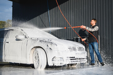 A man washes off the foam while washing the car. A vehicle is engulfed in soapy foam during a car...