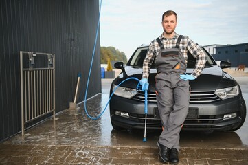 Portrait of a car wash station worker holding a water jet gun next to a clean car