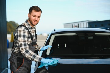 Car detailing - the man holds the microfiber in hand and polishes the car. Selective focus