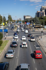A blurred, wide-angle shot of a busy highway intersection on a sunny day. The image captures the dynamic movement of cars and urban life, conveying a sense of bustling city activity