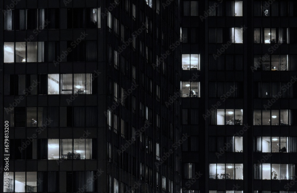 Aufkleber Dark modern office building at night with illuminated windows creating a grid pattern