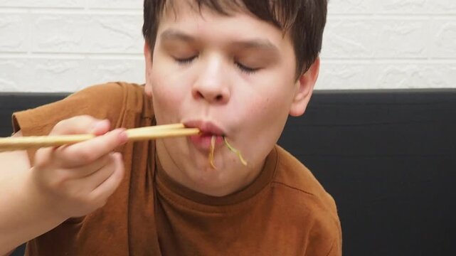 boy eatSchezwan Noodles or Vegetable Hakka Noodles or Chow Mein in white bowl. Schezwan Noodles is indo-chinese cuisine hot dish with udon noodles, vegetables and chilli sauce with meat, Japanese food