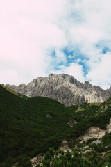 Zerkl&uuml;ftete Felswand erhebt sich &uuml;ber gr&uuml;ne Alpenh&auml;nge unter blauem Himmel