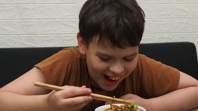 boy eatSchezwan Noodles or Vegetable Hakka Noodles or Chow Mein in white bowl. Schezwan Noodles is indo-chinese cuisine hot dish with udon noodles, vegetables and chilli sauce with meat, Japanese food