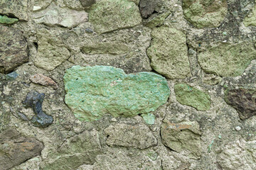 The masonry of an antique wall made of rough dark stones of different sizes with a greenish tint,...