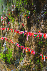 Brightly colored ribbons of wishes are tied on the slope of a mountain waterfall