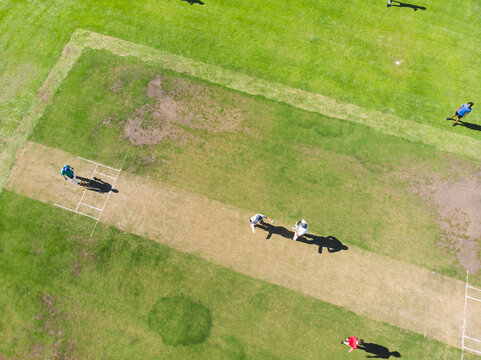 Diverse male cricket team walking on central pitch at sports field with wicket stumps - Powered by Adobe