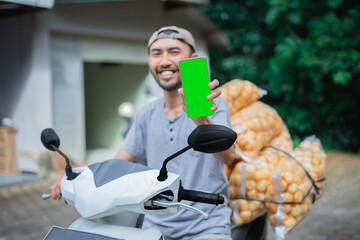 A happy delivery rider shows a smartphone while transporting fresh produce to customers
