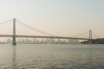 Naklejka premium Suspension bridge, city skyline, hazy sunrise, calm water, travel brochure