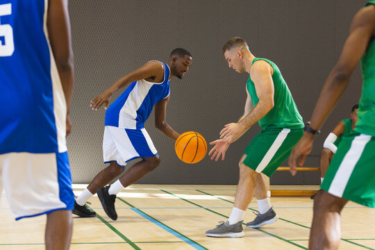 Diverse male athletes in jerseys dribbling and defending on court with green and blue lines