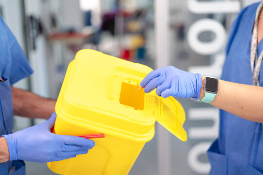 Doctor disposing of contaminated syringe in a sharps container in hospital setting