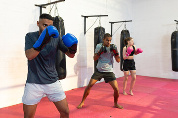 Diverse training partners practicing boxing drills with gloves on mats in gym with heavy bags