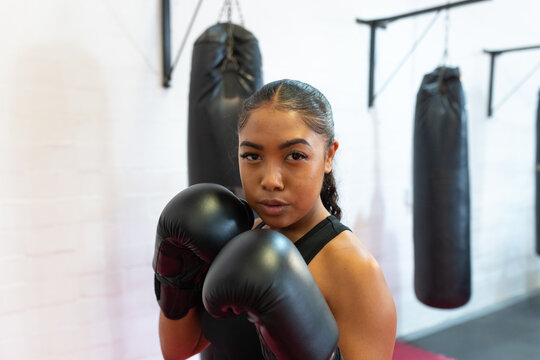 Hispanic woman standing in ready stance at boxing gym with gloves, punching bags
