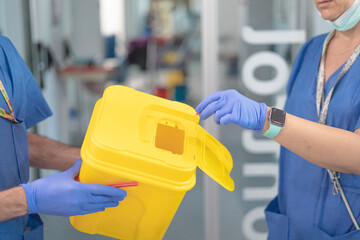 Two healthcare professionals disposing of medical waste in sharps container