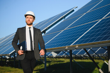 Man in business suit, solar panels on backstage. Client in white helmet standing at solar energy...