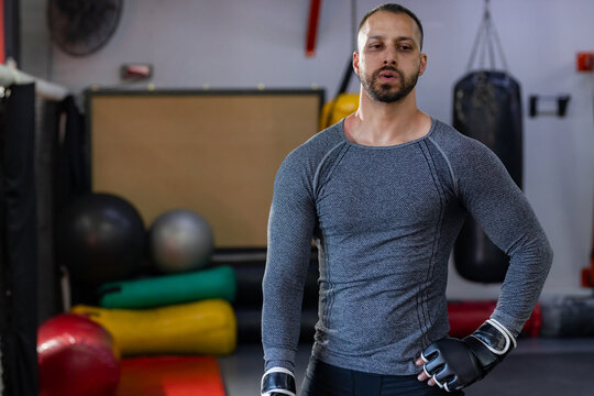 Mid adult indian man pausing in boxing gym between rounds with punching bag, black gloves