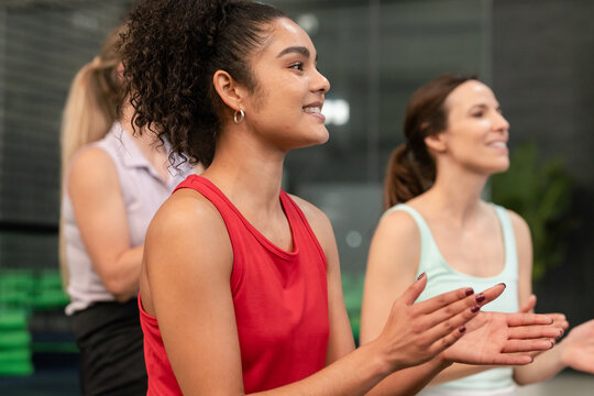 Female fitness group clapping, smiling in gym with stacked green foam mats, copy space