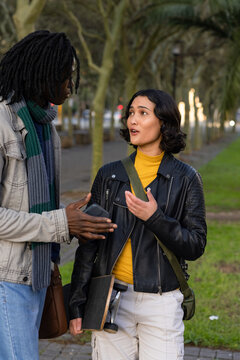 Diverse friends chatting on park pathway while holding smartphone, skateboard