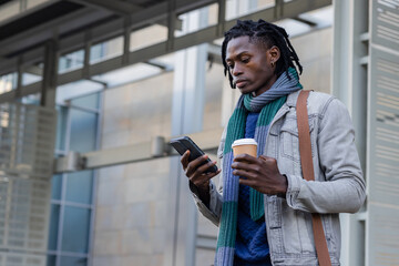 Mid-adult african american man using smartphone under canopy with coffee cup, bag, copy space
