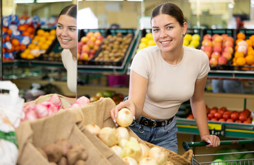 Young woman shopper in casual clothes buys onions at grocery store